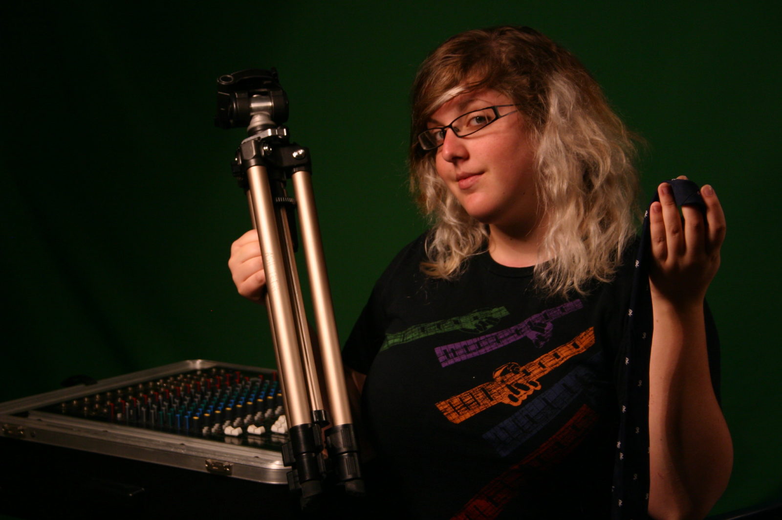 A classmate from Deanna's photography class holds a camera tripod in front of a green backdrop