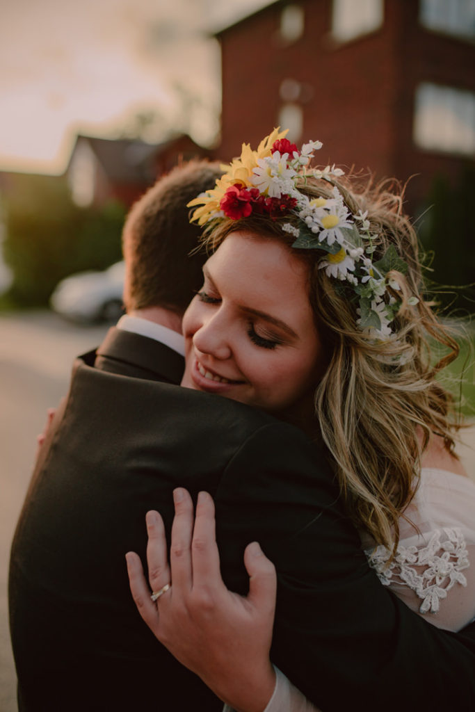 Bride in a beautiful red, white, and yellow flower crown hugs her groom in celebration of their elopement