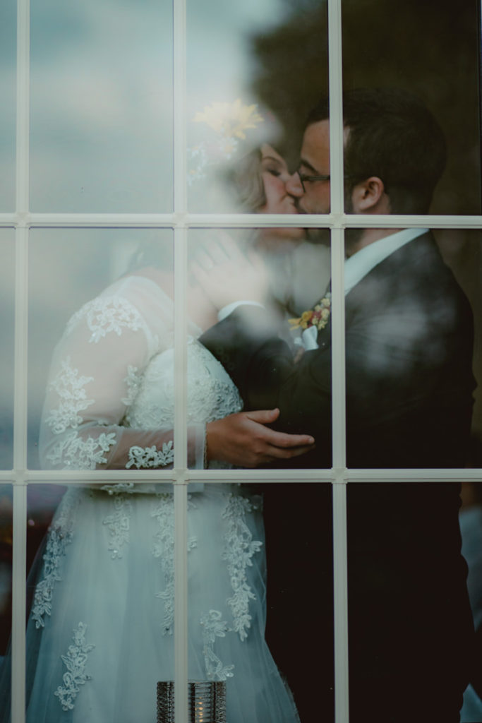 Bride in a flower crown kisses her groom behind a window the day of their Prince Edward County elopement