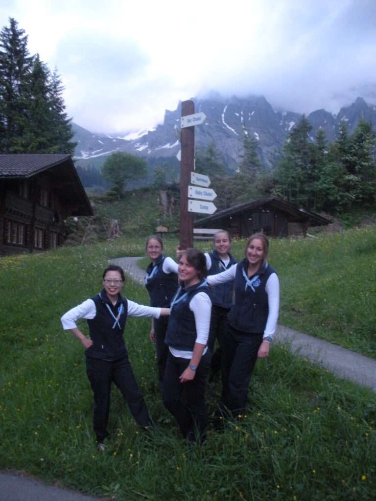 Deanna and four other volunteers hang around a wooden direction pole in the grass in Switzerland 