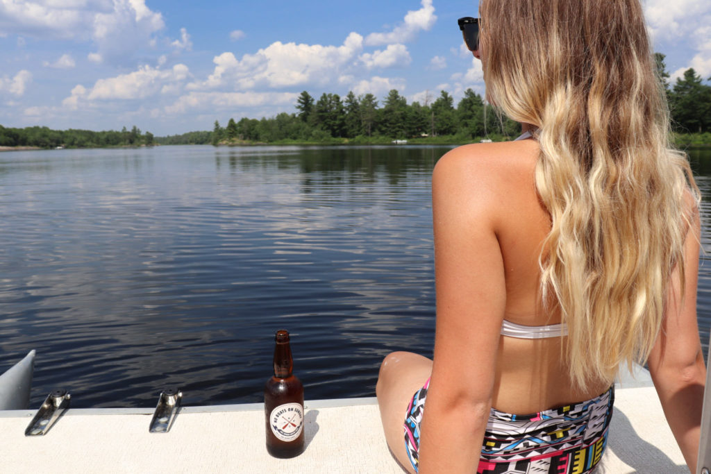Deanna Way sits on the back of a boat in Ontario with a cider by her side, illustrating exactly why she would later become “That Cider Girl” on Instagram
